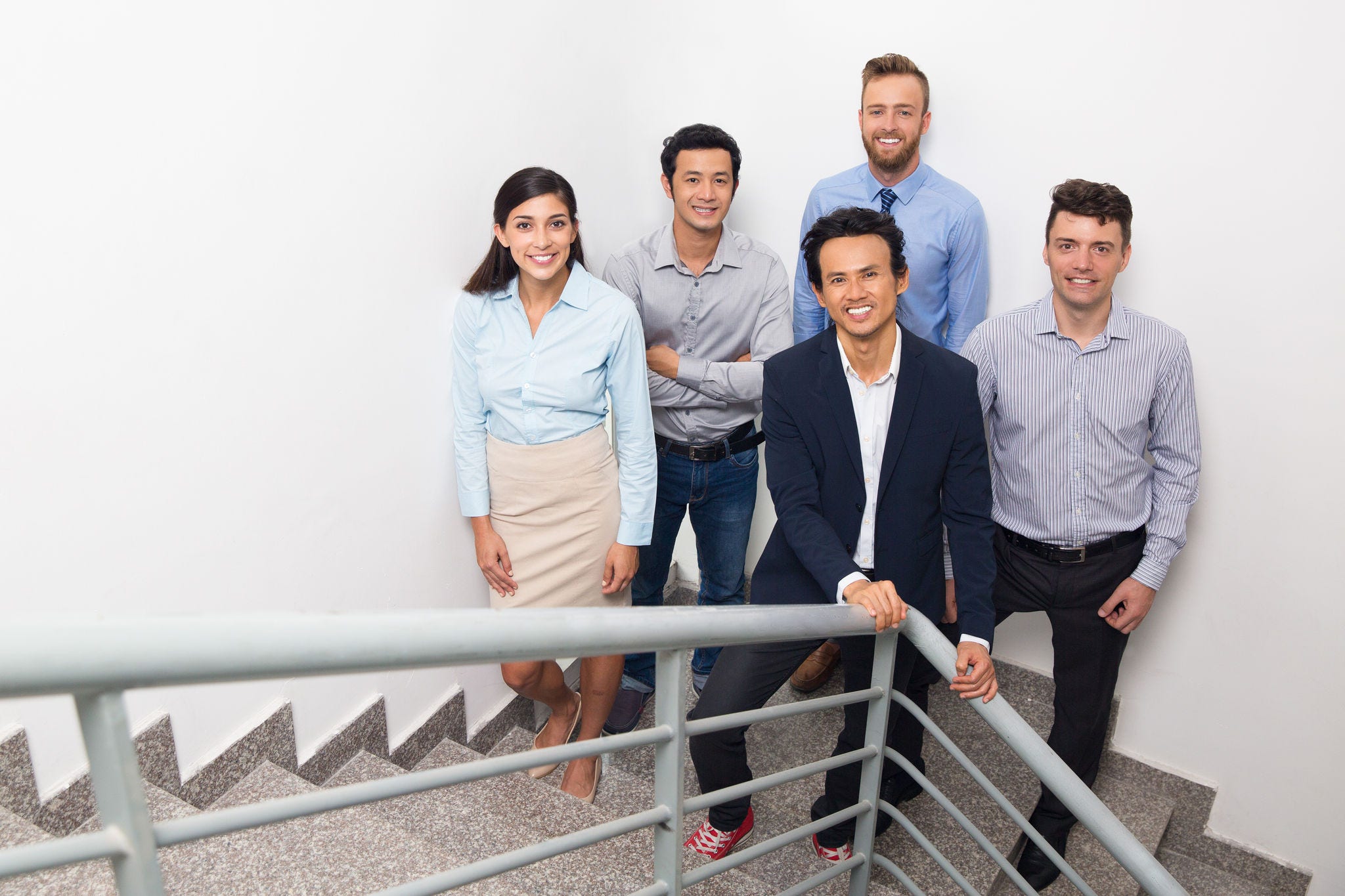 Four smiling middle-aged business people gathering on office stairway, standing and looking at camera. High angle distant view.