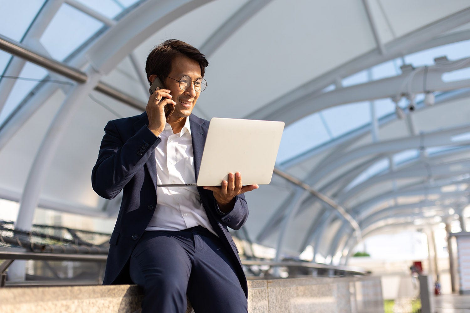 Make your mark Asian confidently business man in glasses and suit working on laptop and mobole phone outdoor in city.