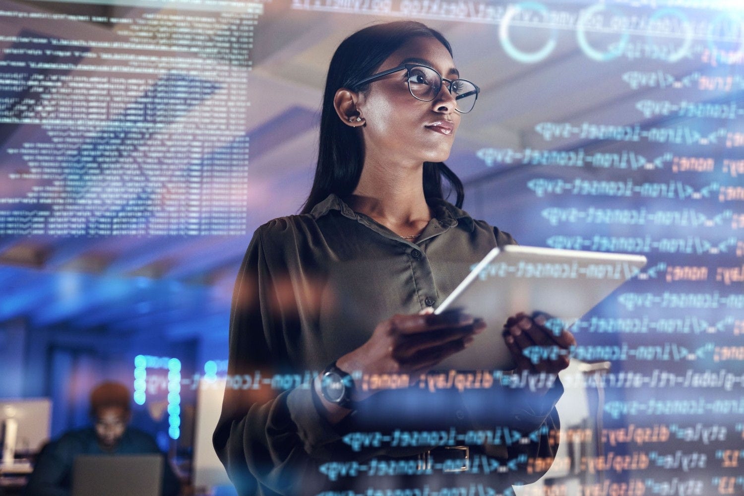 Person holding a tablet while working with code and data displayed on digital screens.