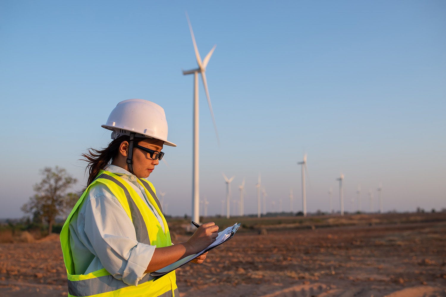 Women engineer working and holding the report at wind turbine farm