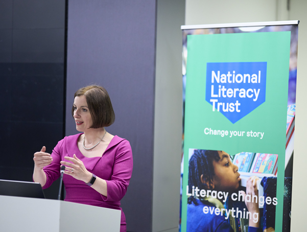 A person performing public speaking next to a National Literacy Trust banner