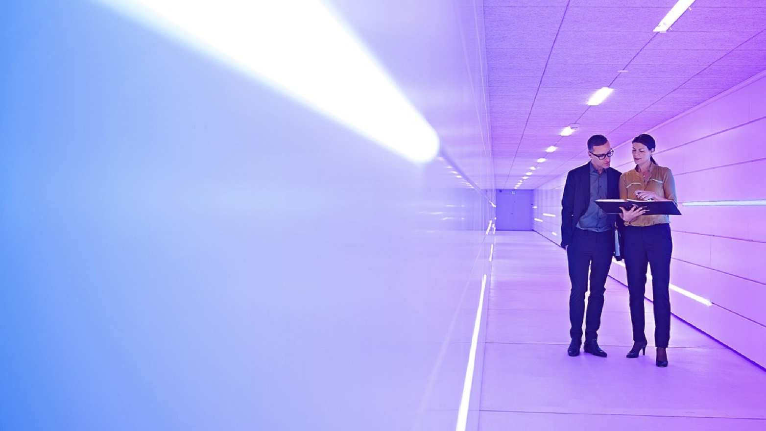 man and woman talking over a tablet as they walk down a corridor